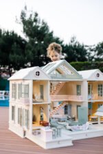 Handcrafted wooden dollhouse with miniature furniture and details, displayed in a minimal setting.