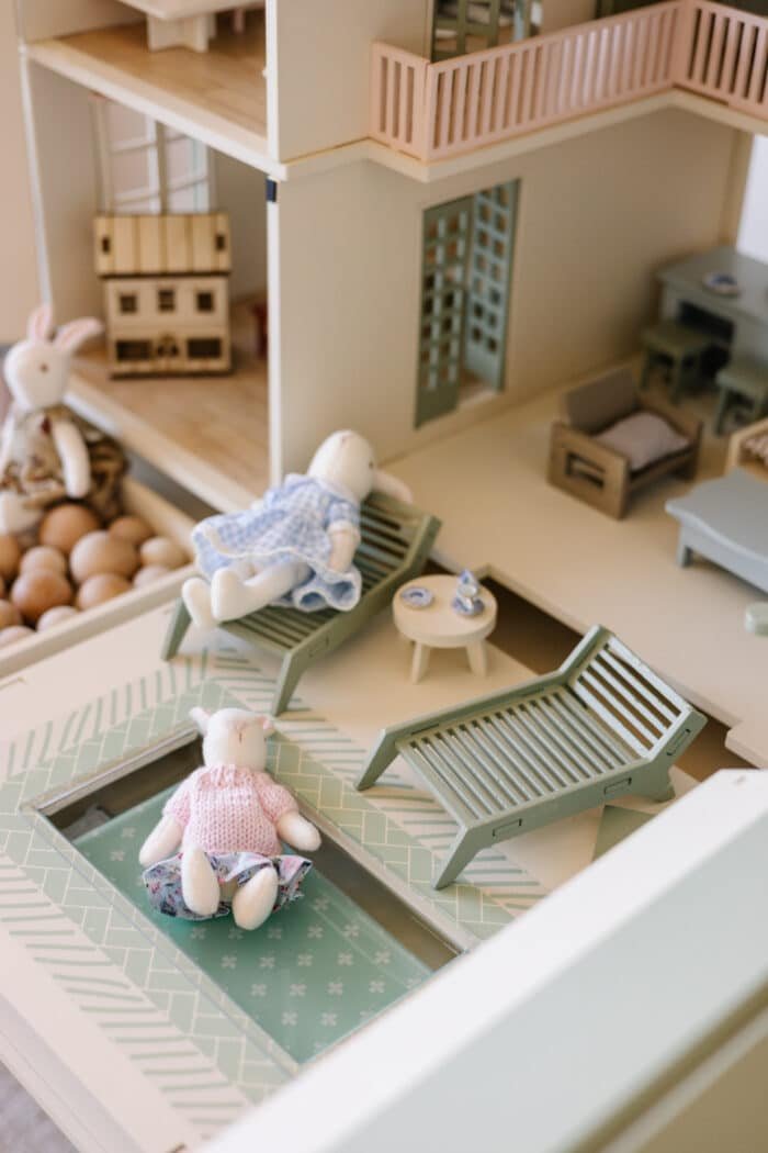 Handcrafted wooden dollhouse with miniature furniture and details, displayed in a minimal setting.