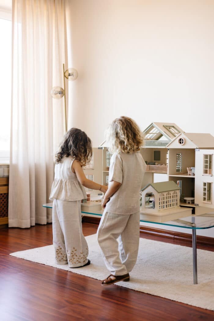 Handcrafted wooden dollhouse with miniature furniture and details, displayed in a minimal setting.