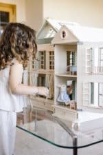 Handcrafted wooden dollhouse with miniature furniture and details, displayed in a minimal setting.