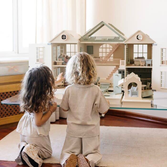 Handcrafted wooden dollhouse with miniature furniture and details, displayed in a minimal setting.