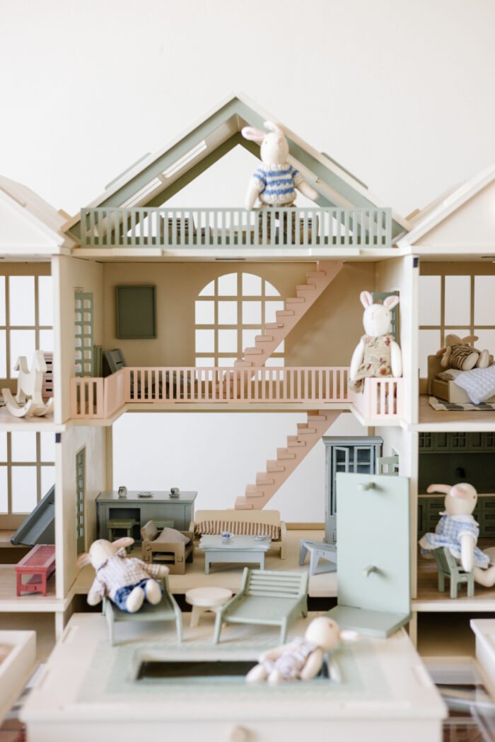 Handcrafted wooden dollhouse with miniature furniture and details, displayed in a minimal setting.