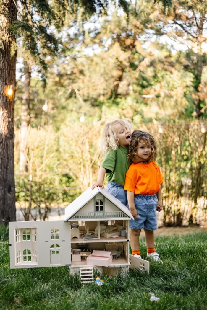 Victorian-style handcrafted white wooden dollhouse by Little Forest Animals, photographed outdoors on green grass in natural light.